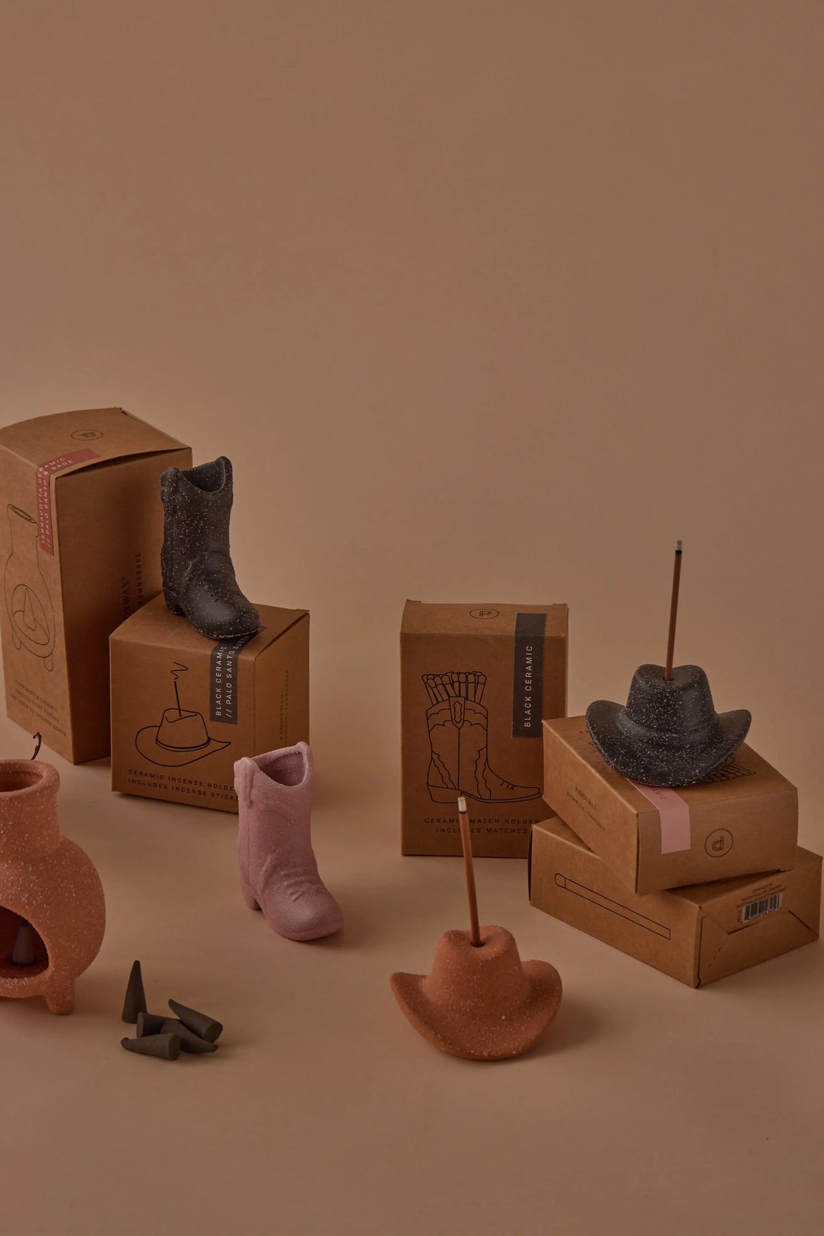 Palo Santo Suede - Incense Holders shaped like cowboy boots and hats are arranged with incense sticks on cardboard boxes, evoking a Nashville-inspired decor scene against a beige background.