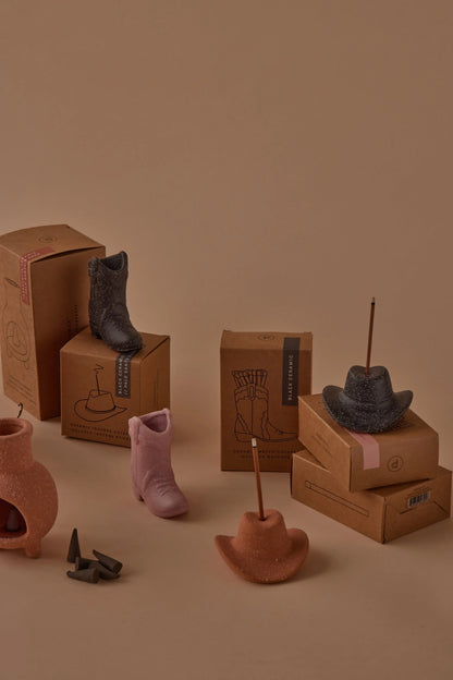 Palo Santo Suede - Incense Holders shaped like cowboy boots and hats are arranged with incense sticks on cardboard boxes, evoking a Nashville-inspired decor scene against a beige background.