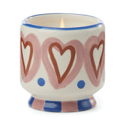 The Rosewood Vanilla - A Dopo 8 oz Candle comes in a hand-painted white ceramic holder featuring pink hearts, blue dots, and blue and pink stripes—perfect for enjoying Mediterranean-inspired scents.