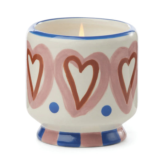 The Rosewood Vanilla - A Dopo 8 oz Candle comes in a hand-painted white ceramic holder featuring pink hearts, blue dots, and blue and pink stripes—perfect for enjoying Mediterranean-inspired scents.