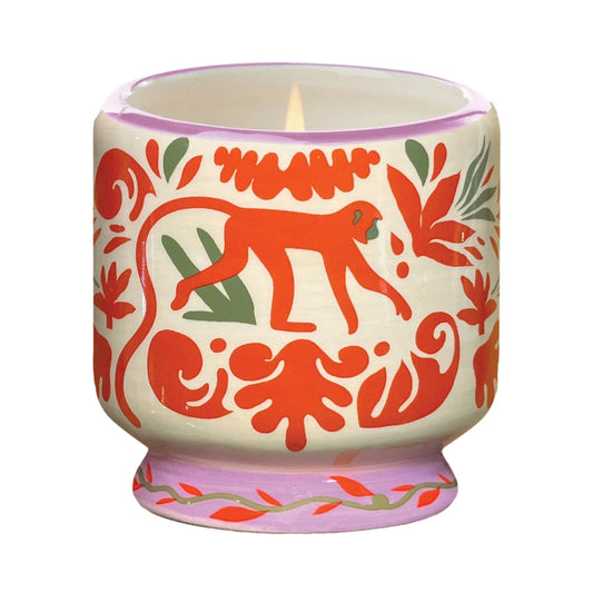 The Coconut & Amber - A Dopo 8 oz Candle comes in a lit ceramic holder with red and green animal and leaf patterns, featuring a central red monkey—perfect for fans of bold fragrance candles.