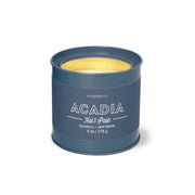 A Parks Collection Acadia - Parks 6 oz Tin Candle with blue tin, yellow wax, and Seagrass + Driftwood scent is shown against a white background.