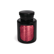 The Linen & Orris - Apothecary Noir 8 oz Candle is a black glass apothecary candle with a round lid and a metallic red label featuring decorative text on the front, displayed against a white background.