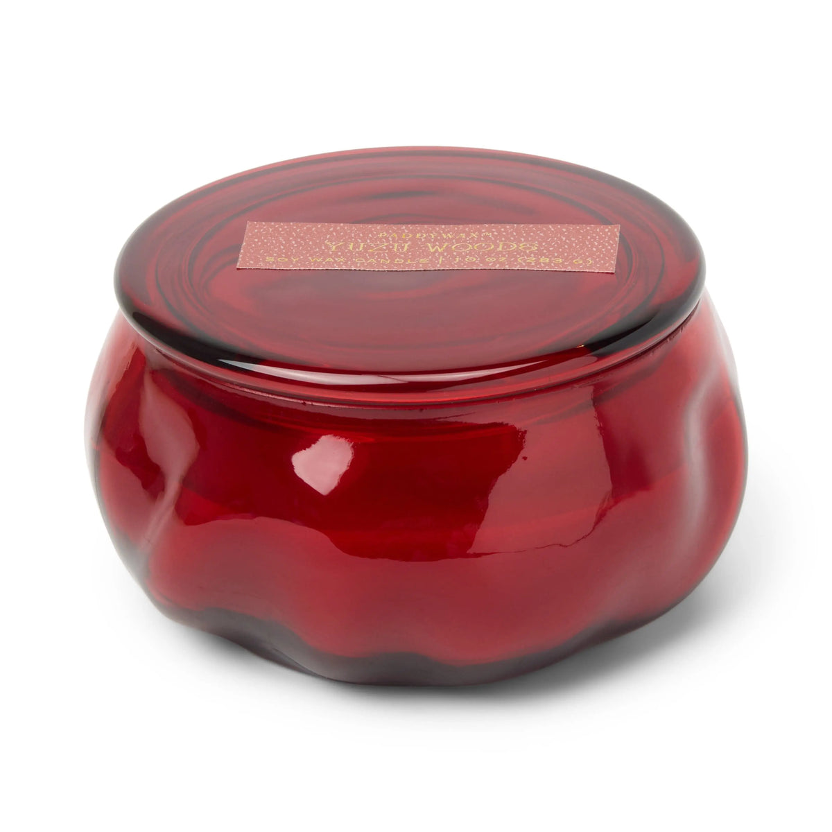 A round, deep red glass jar with a matching lid and a gold label on top, the Yuzu Woods - Basalt 10 oz Candle is strikingly displayed against a white background.