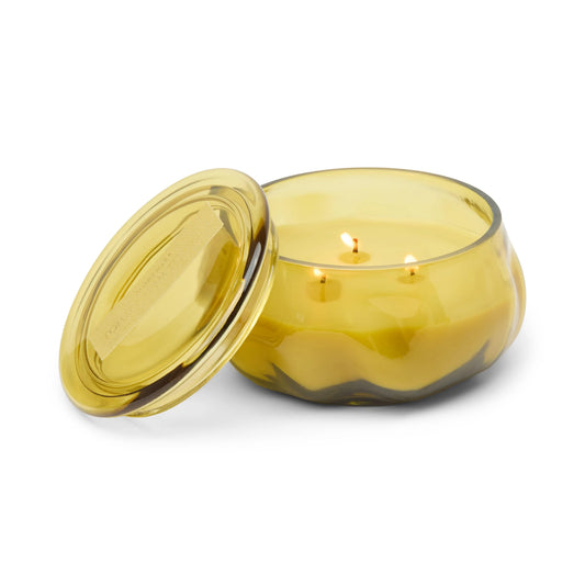 A yellow Tobacco Patchouli - Basalt 10 oz Candle with a wavy glass pattern and its lid set beside it, featuring three lit wicks and filling your space with a warm fragrance.