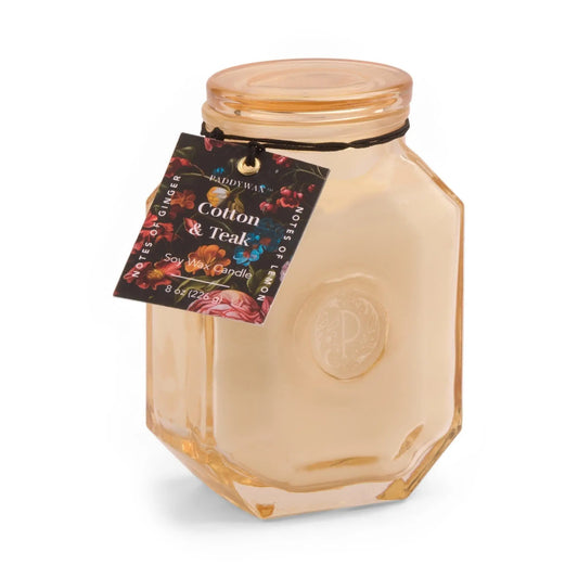 The Cotton + Teak - Botanica 8 oz Candle features beige soy wax in a glass jar with a stylish label—ideal for adding a touch of luxury and inviting fragrance to any space.