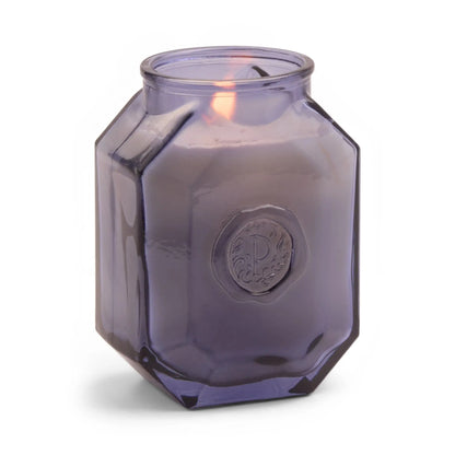 The Sea Salt + Amber Botanica 8 oz Candle glows in a faceted, translucent purple jar with an embossed emblem, perfect for enhancing your home fragrance experience.
