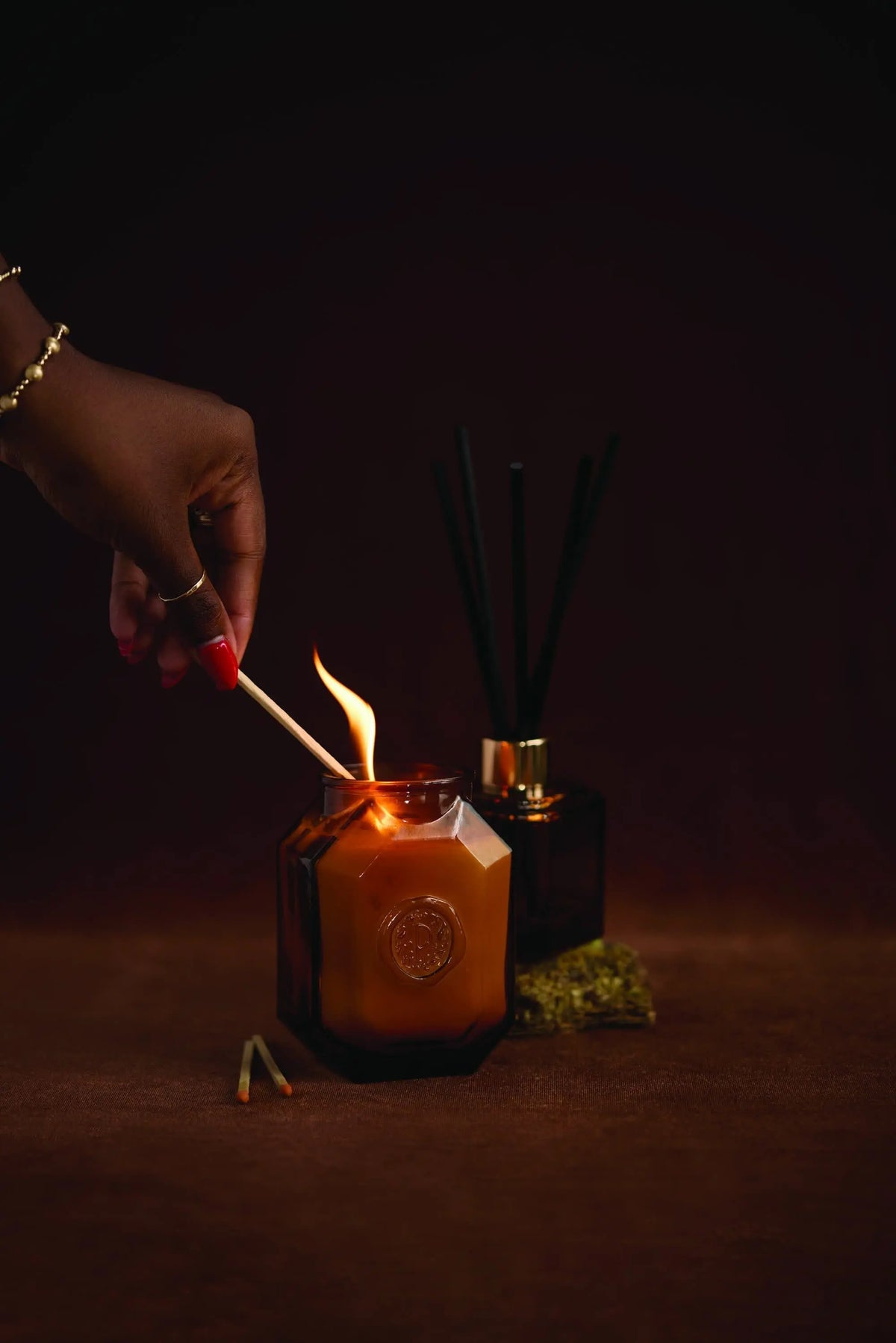 A hand lights the elegant Leather + Smoke - Botanica 8 oz Candle, part of the luxurious Botanica Collection.