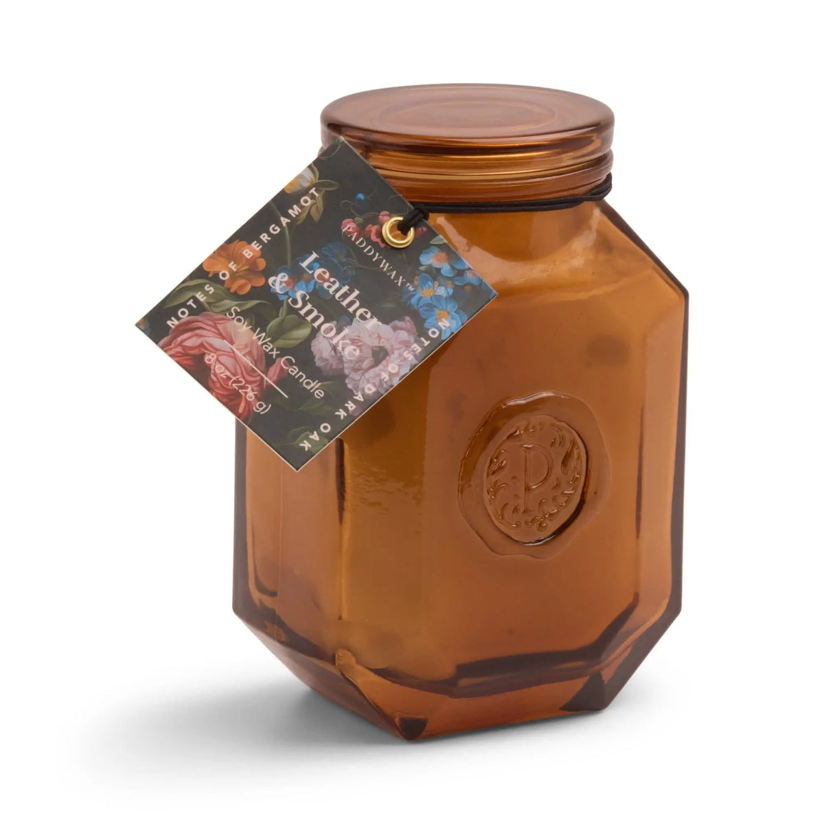 An amber octagonal glass jar with a screw-on lid and floral tag labeled “Leather + Smoke - Botanica 8 oz Candle”—an elegant choice for fans of candles and diffusers.