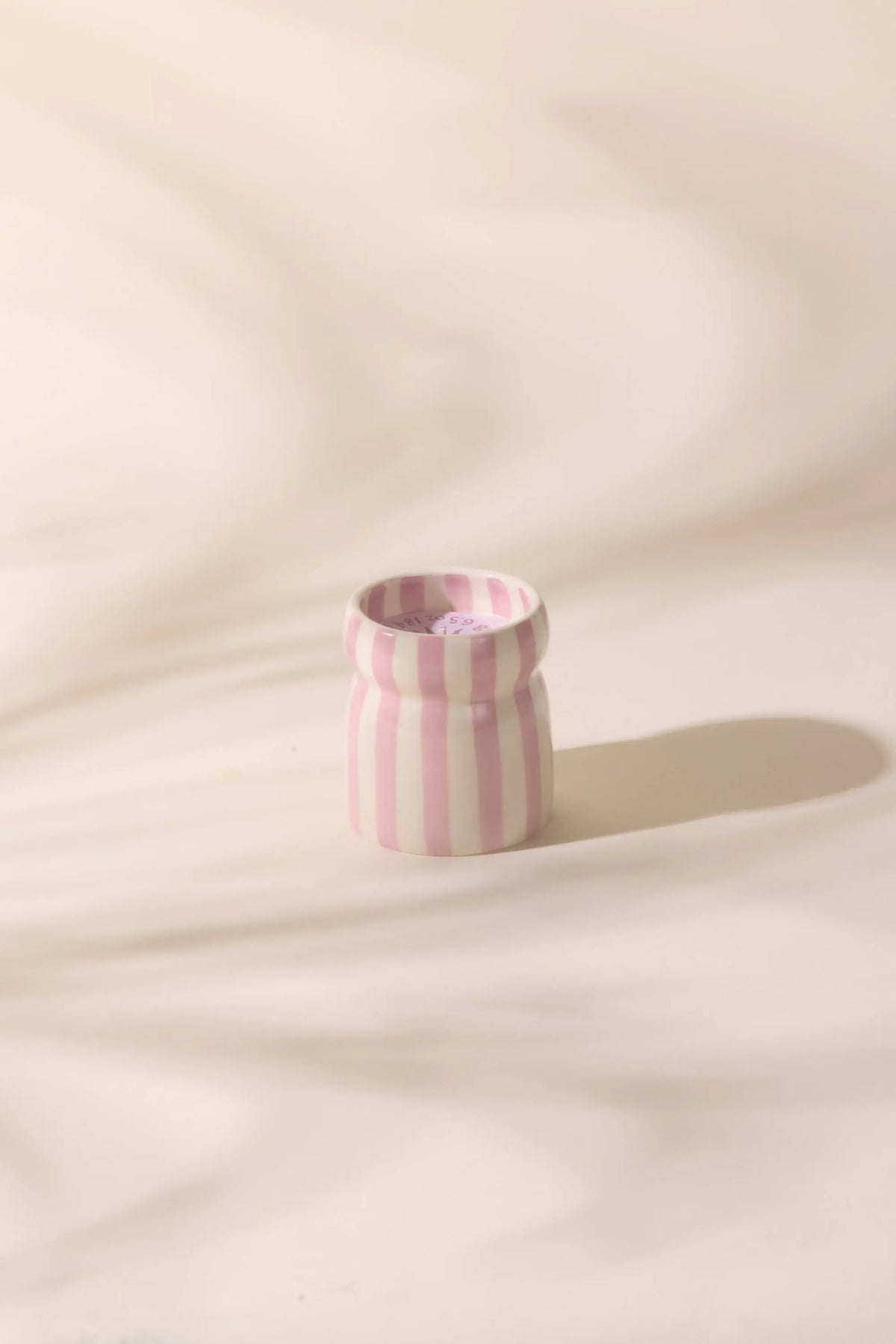 The Grecian Sand - Cabana 6.5 oz Candle features a small ceramic vessel with vertical pink and white stripes, ideal for creating a relaxing coastal vibe with your favorite hand-painted candles or soothing scents.