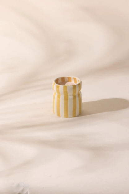 The Gold Coast - Cabana 6.5 oz Candle features a small ceramic vessel with vertical yellow and white stripes, perfect for filling your home with calming coastal scents.