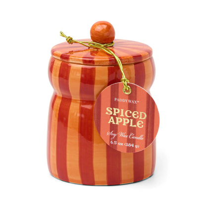 A red and orange striped ceramic jar with a matching lid and a gold string holding a tag labeled “Spiced Apple - Cabana 6.5 oz Candle.” This festive holiday candle fills any space with warmth and an inviting spiced apple fragrance.