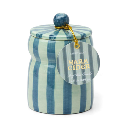 The Warm Cider - Cabana 6.5 oz Candle is a blue and light green striped hand-painted ceramic vessel with a lid, filled with Paddywax soy wax and fragranced with mulled cider. A gold string secures a round tag to the lid.
