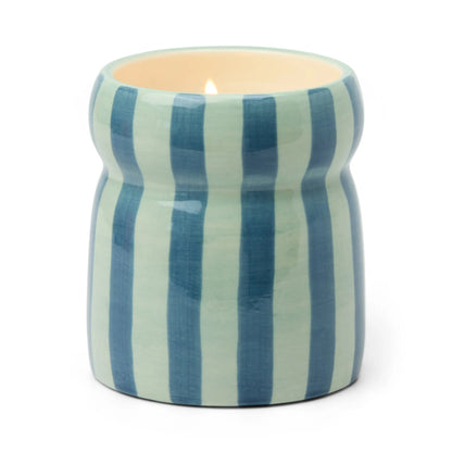The Warm Cider - Cabana 6.5 oz Candle comes in a hand-painted ceramic vessel with vertical blue and light blue stripes. Its curved, glossy holder emits a cozy mulled cider fragrance when lit.