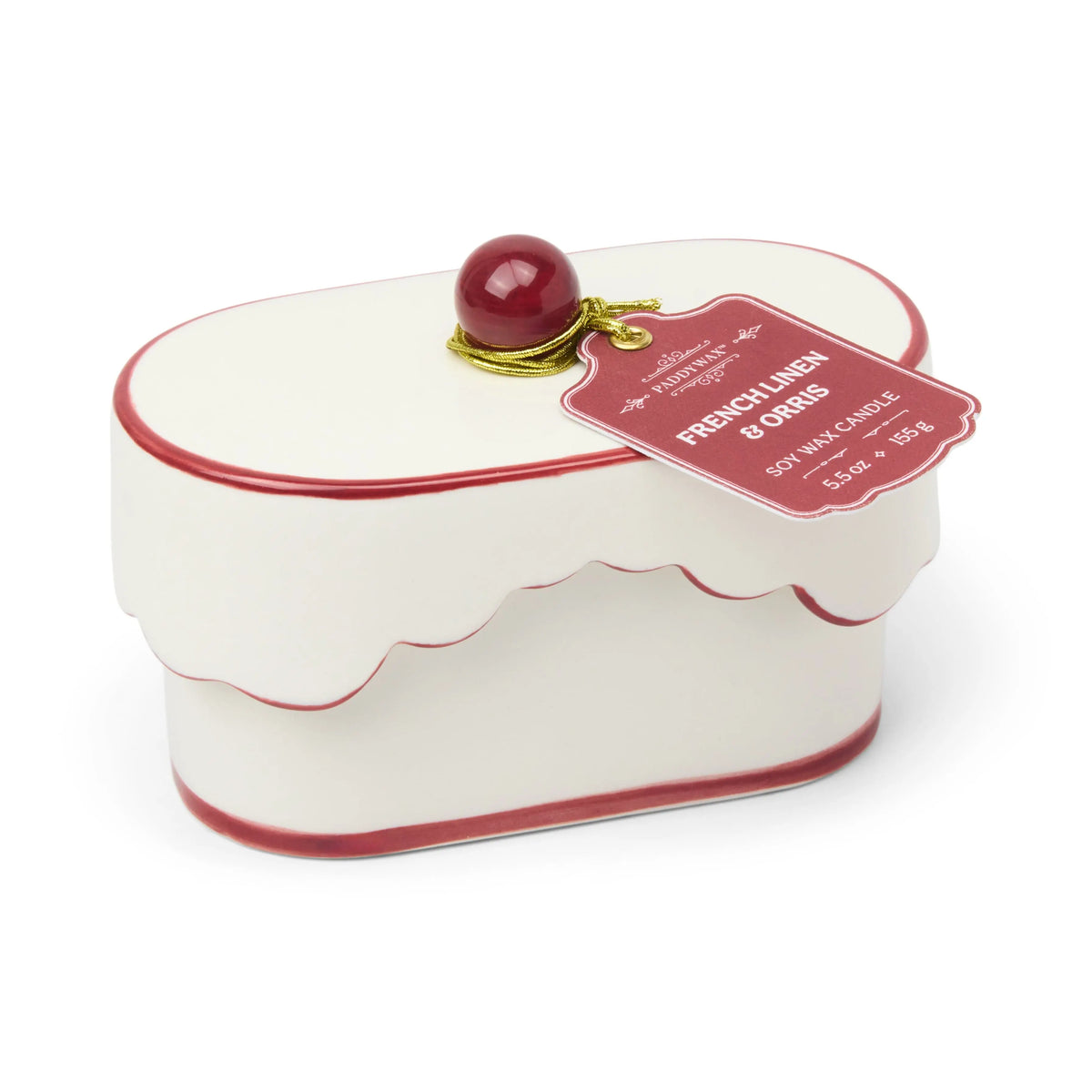 White and red scalloped tin box with a round red knob on top, resembling a cake. A pink tag attached reads French Linen & Orris - Chérie 5.5 oz Ceramic Candle, reminiscent of the elegance found in a porcelain vessel or the soothing fragrance of French linen blends.