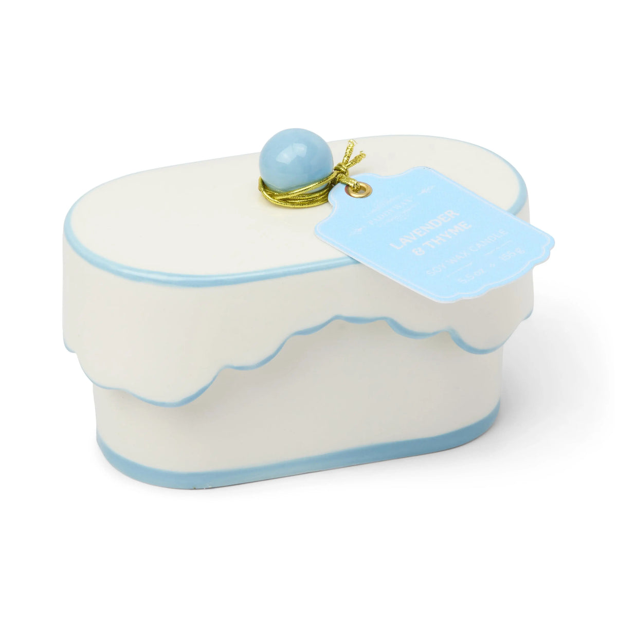 Chérie 5.5 oz Ceramic Candle from Lavender & Thyme features an oval white porcelain vessel with blue trim, a scalloped lid, and a blue knob on top. Hand-painted details decorate the candle, and a blue tag reading "LAVENDER & THYME" is attached with gold string.