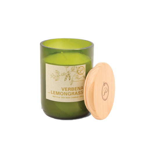 The Verbena + Lemongrass - Eco 8 oz Candle is a green glass soy candle with a botanical design and a wooden lid featuring a decorative logo, placed angled against the jar for added style.