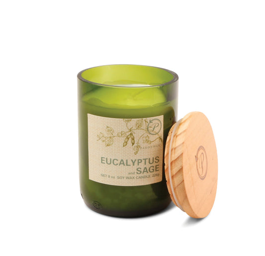 A green glass “Eucalyptus + Sage - Eco 8 oz Candle” with a wooden lid, featuring botanical illustrations and text describing it as soy wax in a recycled vessel.