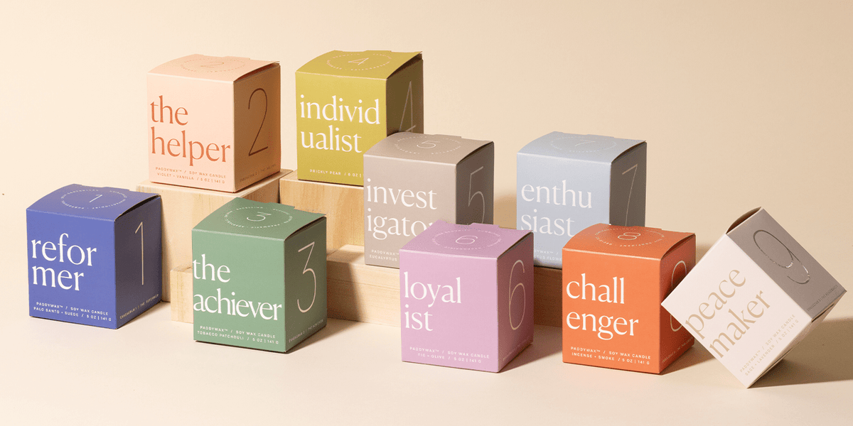 Nine pastel-colored boxes labeled with different personality types (the helper, individualist, investigator, enthusiast, reformer, achiever, loyalist, challenger, peacemaker) are arranged on a wooden display.