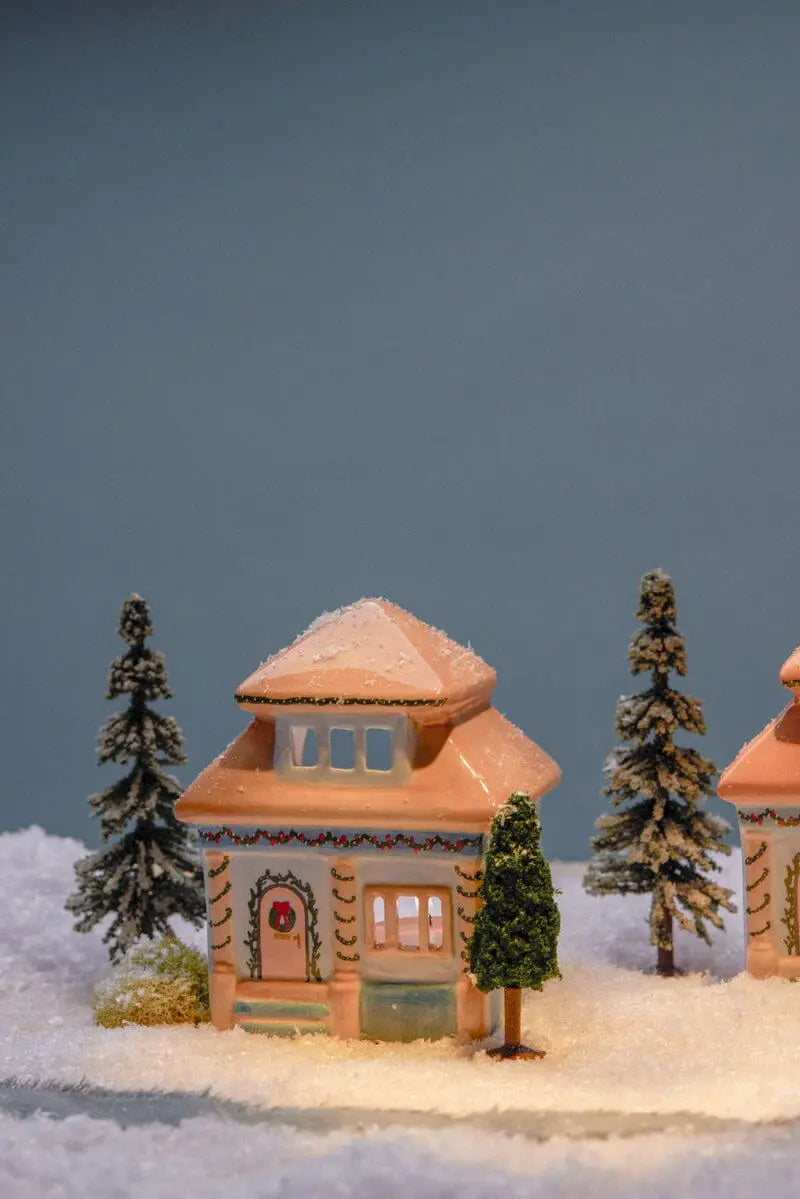 No. 06 The East Side House - Incense & Tea Light Holder, adorned with holiday lights, rests among artificial snow and miniature pine trees against a plain blue background.
