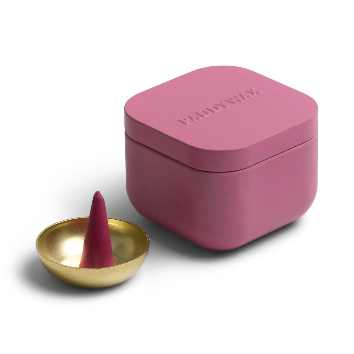 A pink square Pomelo Bay - Metal Incense Tin sits next to a small gold incense cone holder, perfectly showcasing one of their best-selling fragrances with a cone-shaped scented incense cone.