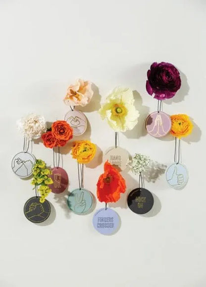 The Tobacco + Vanilla "Love Ya" Impressions Car Fragrance features vibrant artificial flowers on circular tags with embroidered hand gestures, a "Love Ya" phrase, and subtle sandalwood scents—perfect as a unique car accessory.