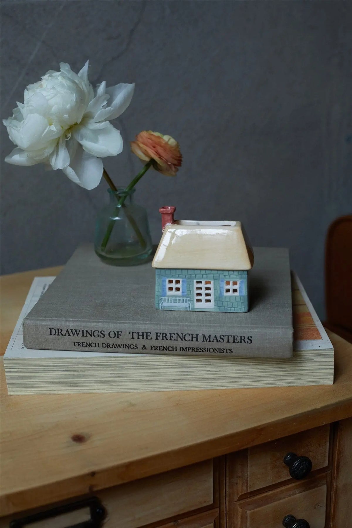 No. 04 The English Cottage—an incense and tea light holder—sits atop two art books near a vase with two flowers, all arranged on a wooden table for charming cottage decor.