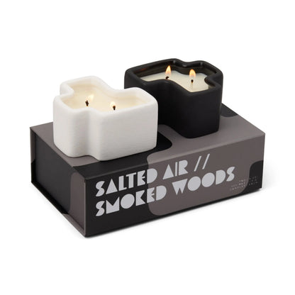 The Salted Air & Smoked Woods - Jigsaw 4 oz Candle Boxed Set includes two uniquely shaped candles—one white and one black—nestled inside a modern, minimalist box. Each candle features three wicks, while the sleek packaging highlights the sophisticated scents of Salted Air and Smoked Woods.