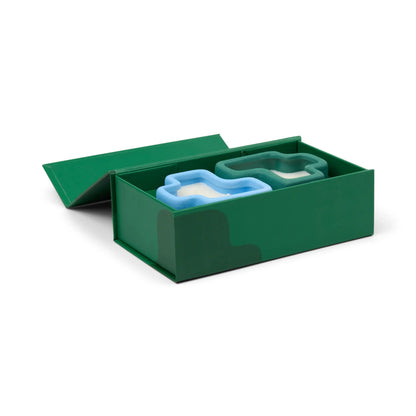 A green box with its lid partially open, revealing a Wild Mint & Misted Lime - Jigsaw 4 oz Candle Boxed Set inside—perfect for elevating your at-home spa experience.