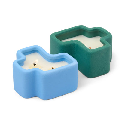 Two abstract, irregularly shaped candles in textured ceramic holders—one in light blue and the other in dark green—both with visible wicks and white wax, placed side by side on a white background. The Wild Mint & Misted Lime - Jigsaw 4 oz Candle Boxed Set features the refreshing scents of Misted Lime and invigorating Wild Mint to elevate any space.