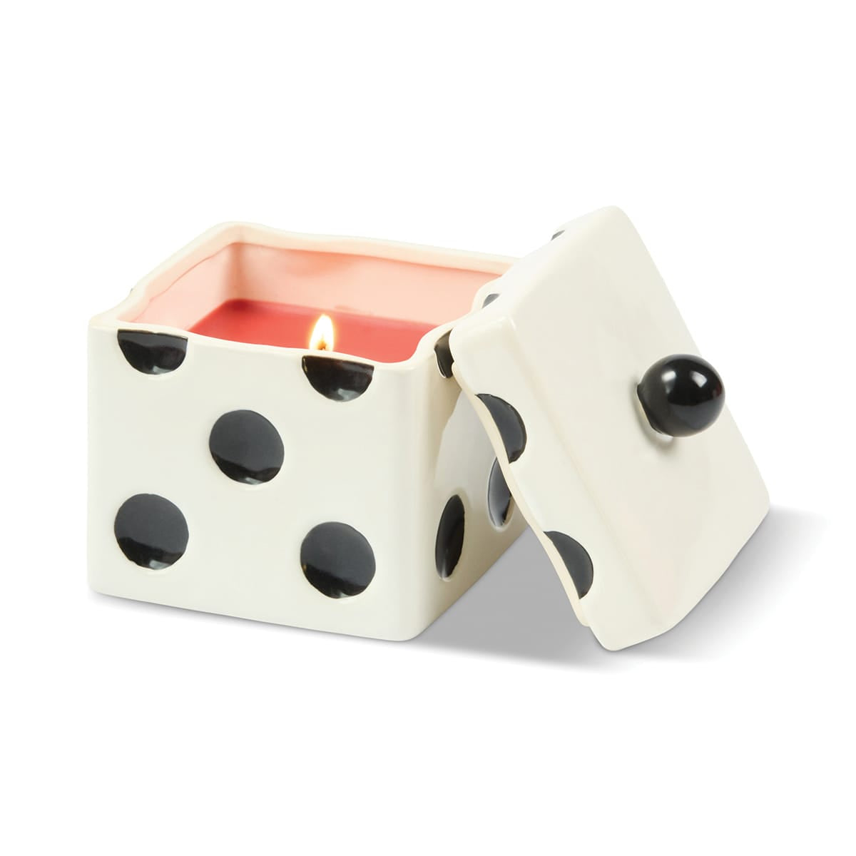 A lit Tobacco Patchouli - Lucky Dice 10 oz Candle in a white ceramic dice-shaped vessel with black dots, with the lid leaning against the side.