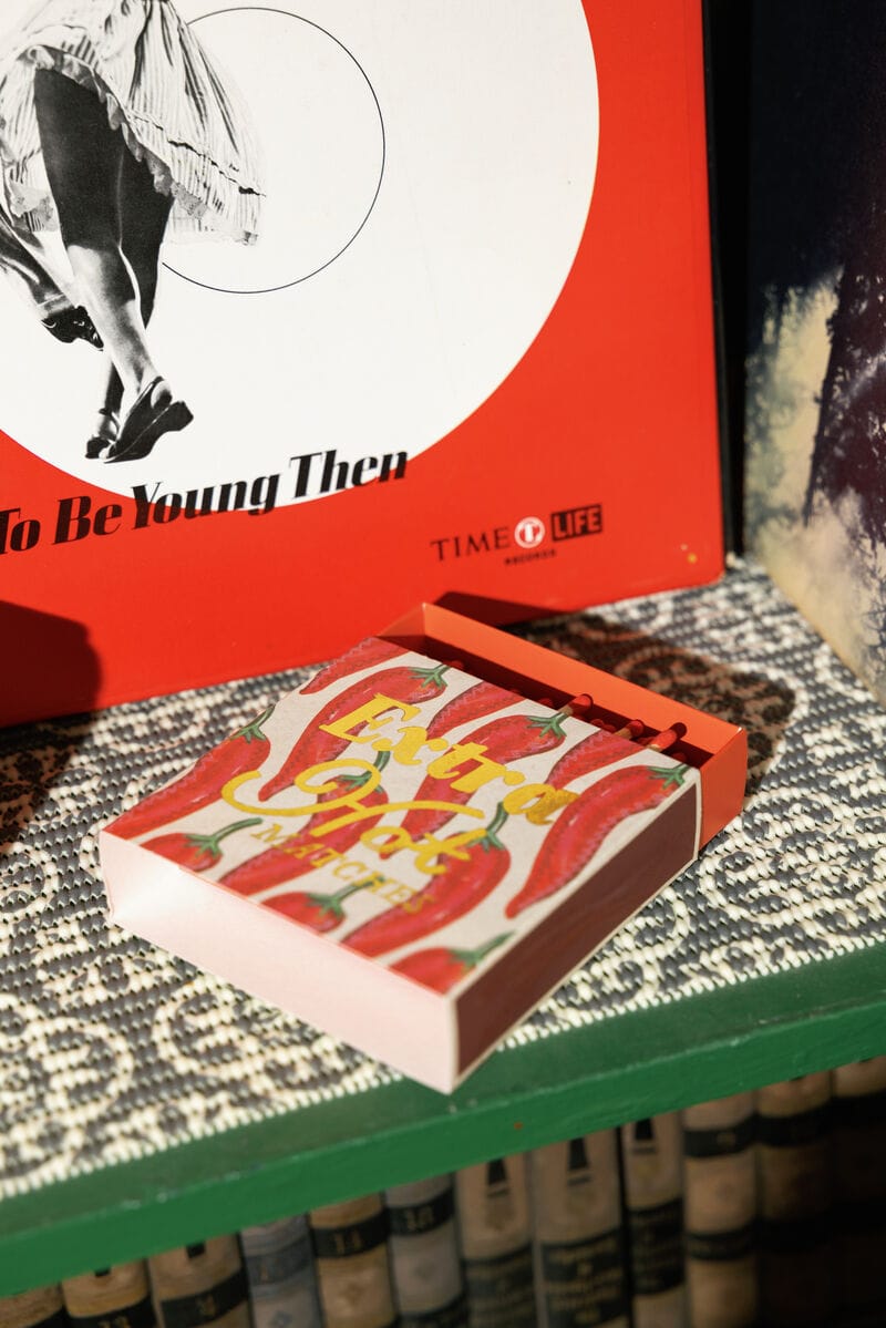 A red Extra Hot - Square Boxed Matches sits on a patterned surface, making a bold host gift in front of a red Time Life book with a black-and-white image of dancing legs.