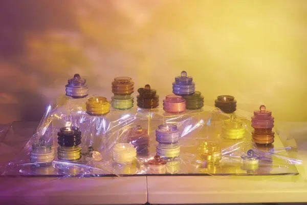 Stacks of vibrant, translucent circles rest on a reflective surface draped in clear plastic, illuminated by yellow and purple light—echoing the warm glow of the Baltic Ember - Beam 3 oz Candle.