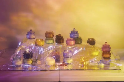Stacks of vibrant, translucent circles rest on a reflective surface draped in clear plastic, illuminated by yellow and purple light—echoing the warm glow of the Baltic Ember - Beam 3 oz Candle.
