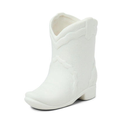 A white ceramic object shaped like a cowboy boot, featuring textured details and inspired by Nashville décor, sits on a white background—capturing the spirit of western fragrances found in the Smoked Pistachio - Nashville Boot oz Candle.