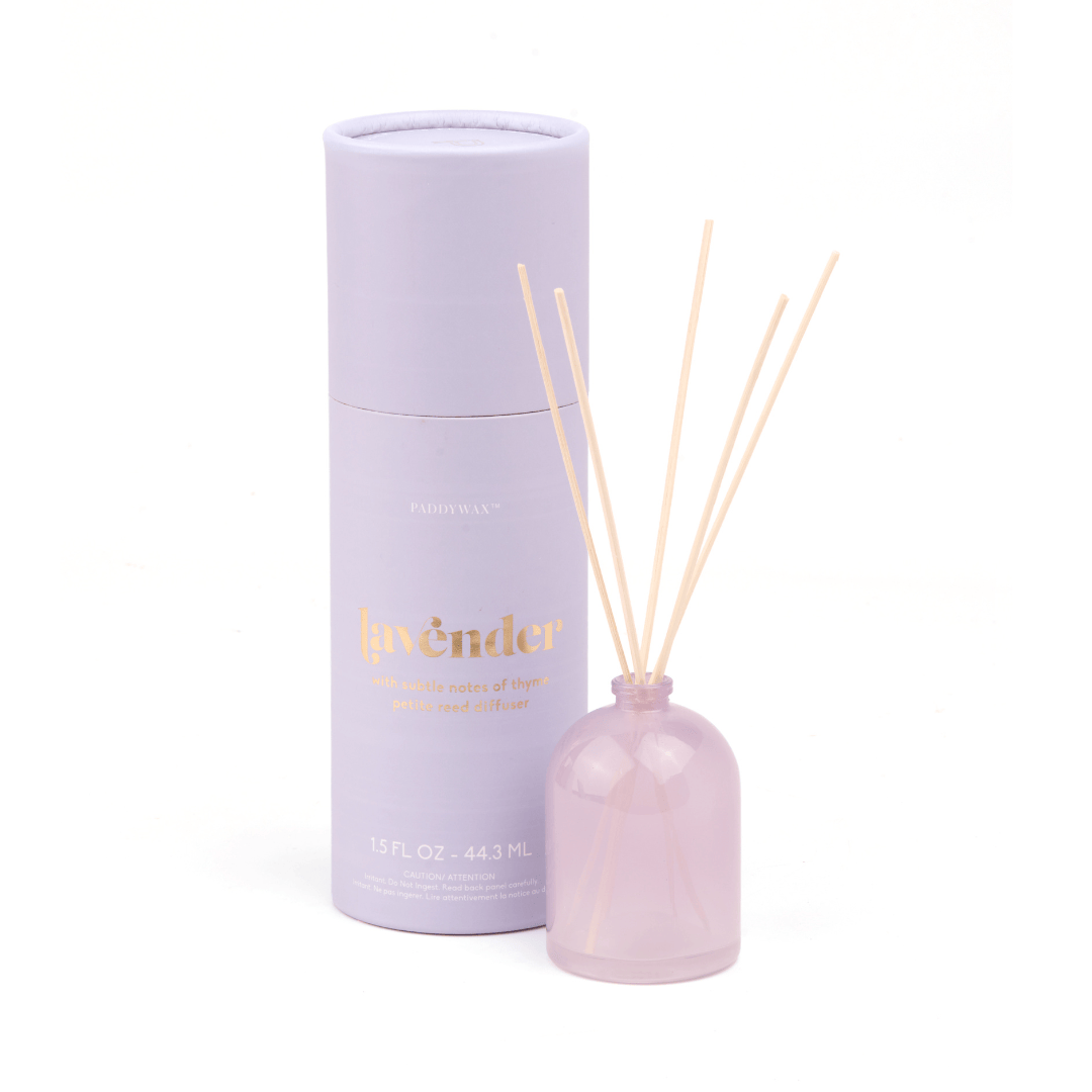 The Lavender - 1.5 oz Diffuser features a milky glass bottle with reeds and comes in a light purple cylindrical box labeled “lavender” in gold—both set against a white background, making it a perfect giftable fragrance.