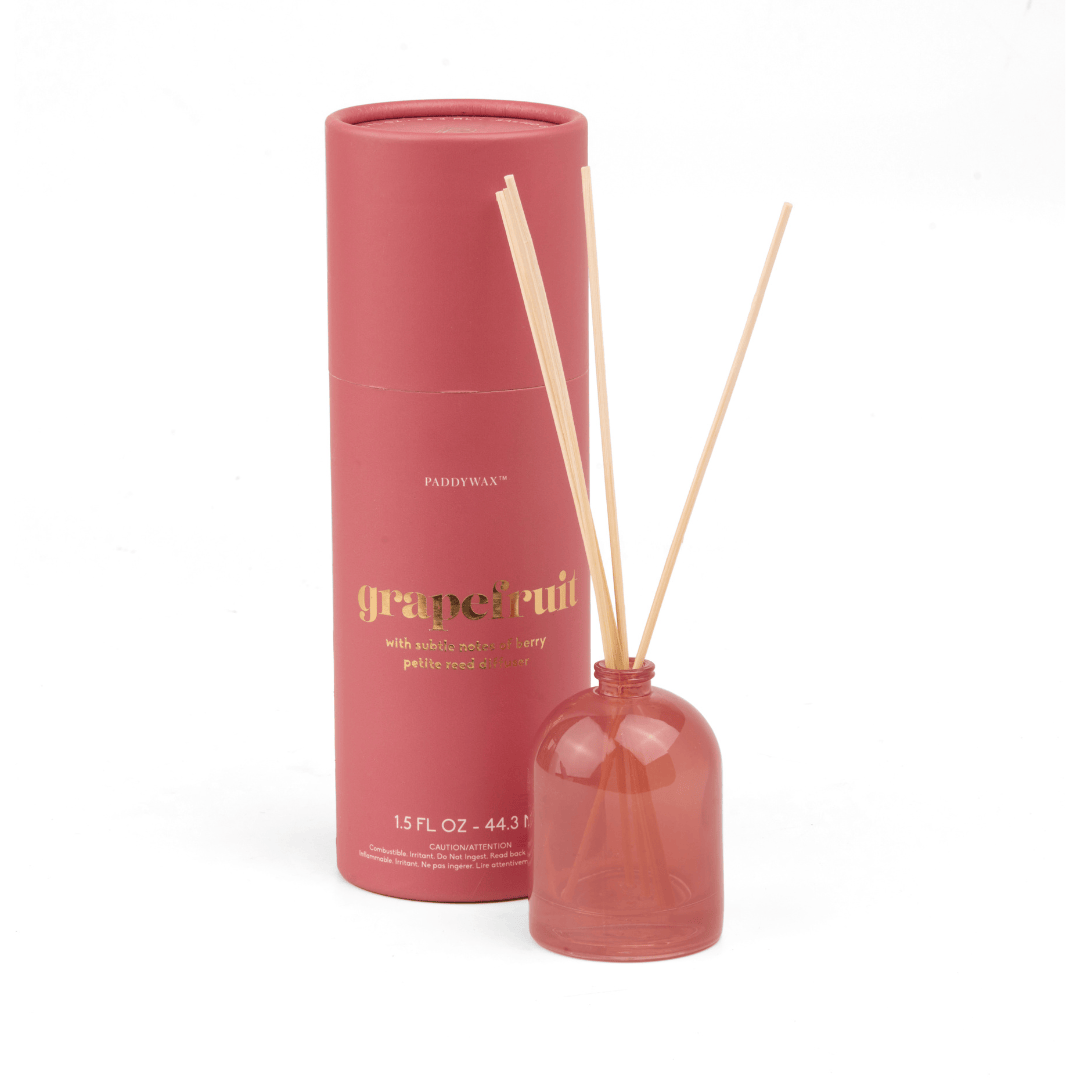 A pink milky glass Grapefruit - 1.5 oz Diffuser with three wooden reeds stands before a matching giftable tube labeled "grapefruit" in gold letters, with additional product details in smaller print on the packaging.
