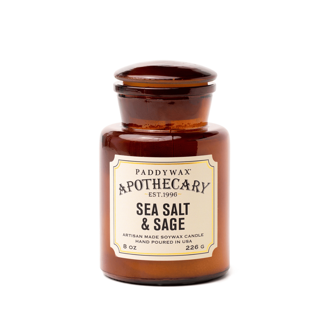 A brown amber glass jar labeled "Sea Salt + Sage - Apothecary 8 oz Candle" evokes a vintage-inspired fragrance reminiscent of classic apothecary bottles.
