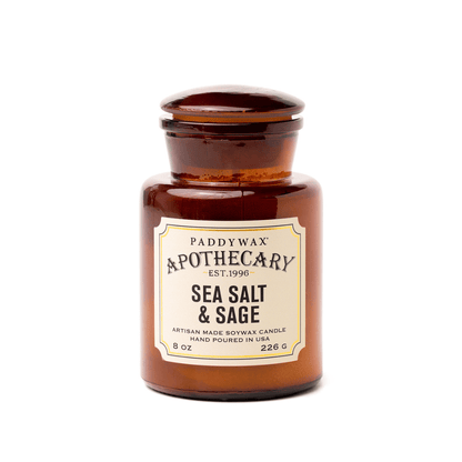 A brown amber glass jar labeled "Sea Salt + Sage - Apothecary 8 oz Candle" evokes a vintage-inspired fragrance reminiscent of classic apothecary bottles.