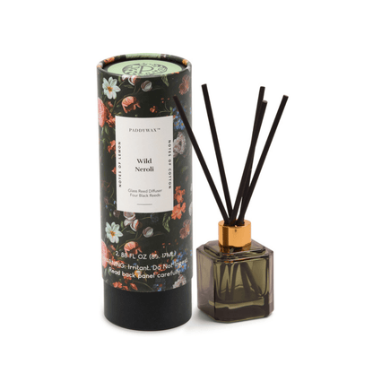 The Wild Neroli - Botanica Diffuser 2.88 oz, featuring black reeds, is shown next to its floral-patterned cylindrical packaging.
