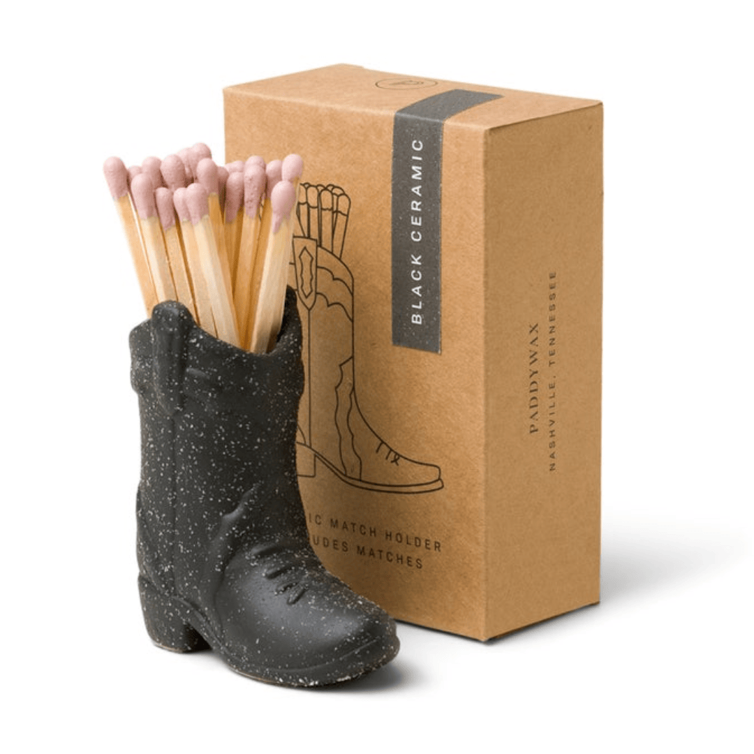The Cowboy Boot Match Holder - Black, filled with matches, sits before a brown box featuring boot artwork and product details—an ideal Nashville gift or stylish Western decor accent.