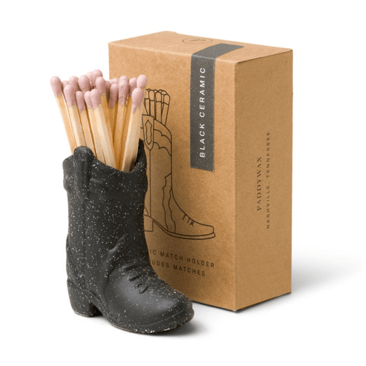 The Cowboy Boot Match Holder - Black, filled with matches, sits before a brown box featuring boot artwork and product details—an ideal Nashville gift or stylish Western decor accent.