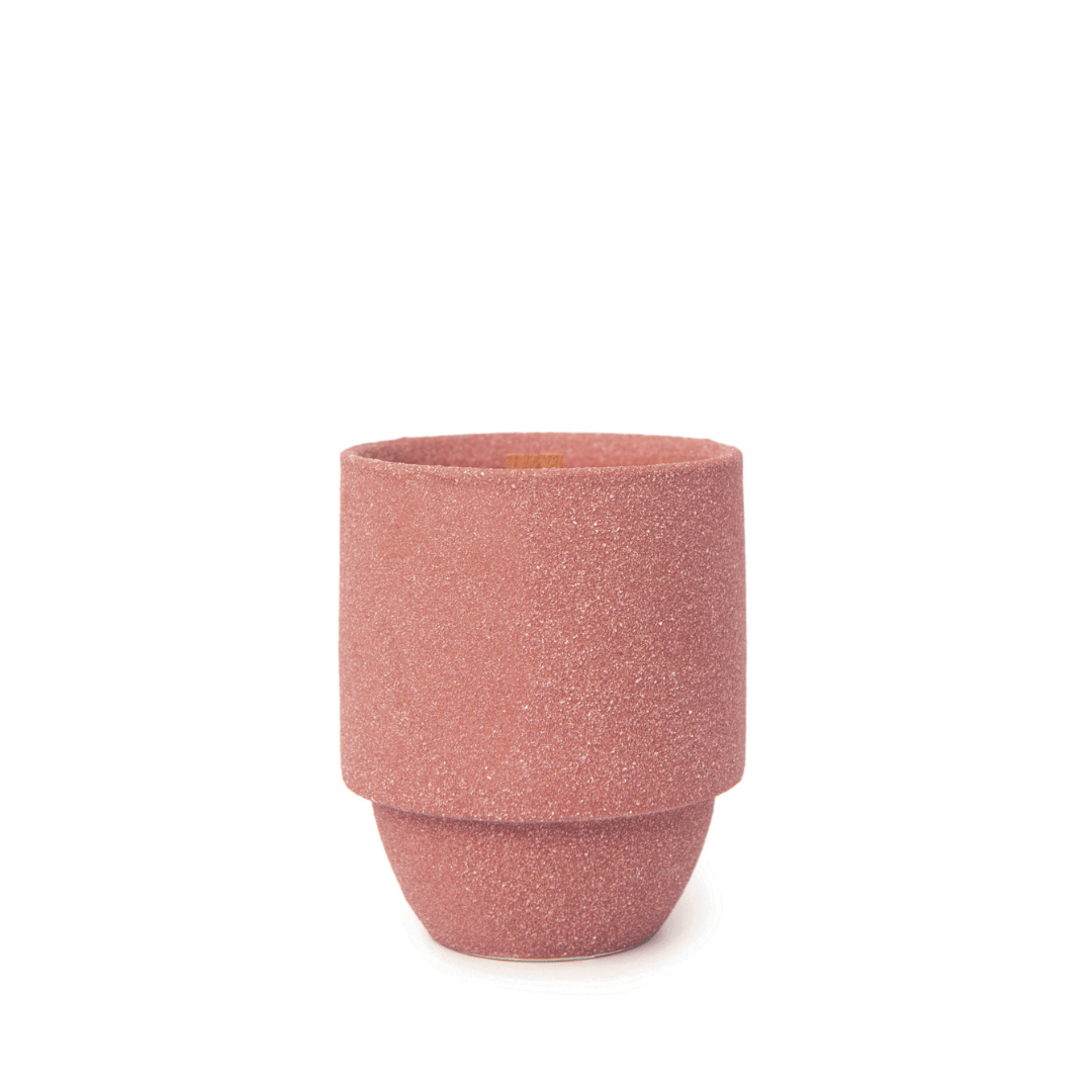 A matte pink ceramic cup with a unique shape is shown centered on white—ideal for enjoying the woody Redwood and Lily scent of the Redwoods - Parks 11 oz Candle.