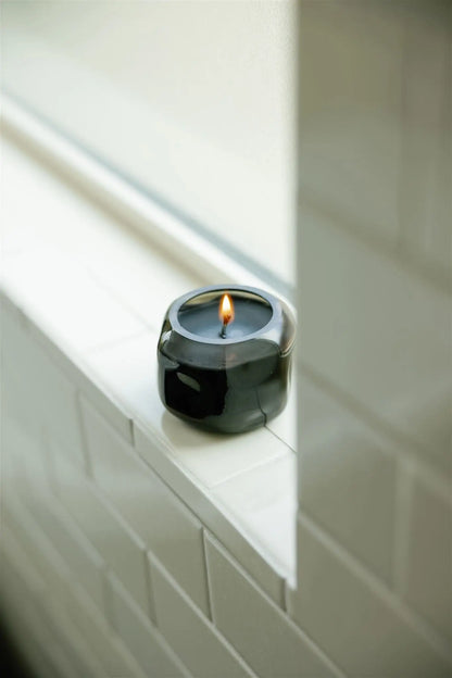 A Basalt 5 oz Palo Santo Suede candle glows on a white tiled windowsill, filling the calm, minimalist space with its subtle smoky wood fragrance.
