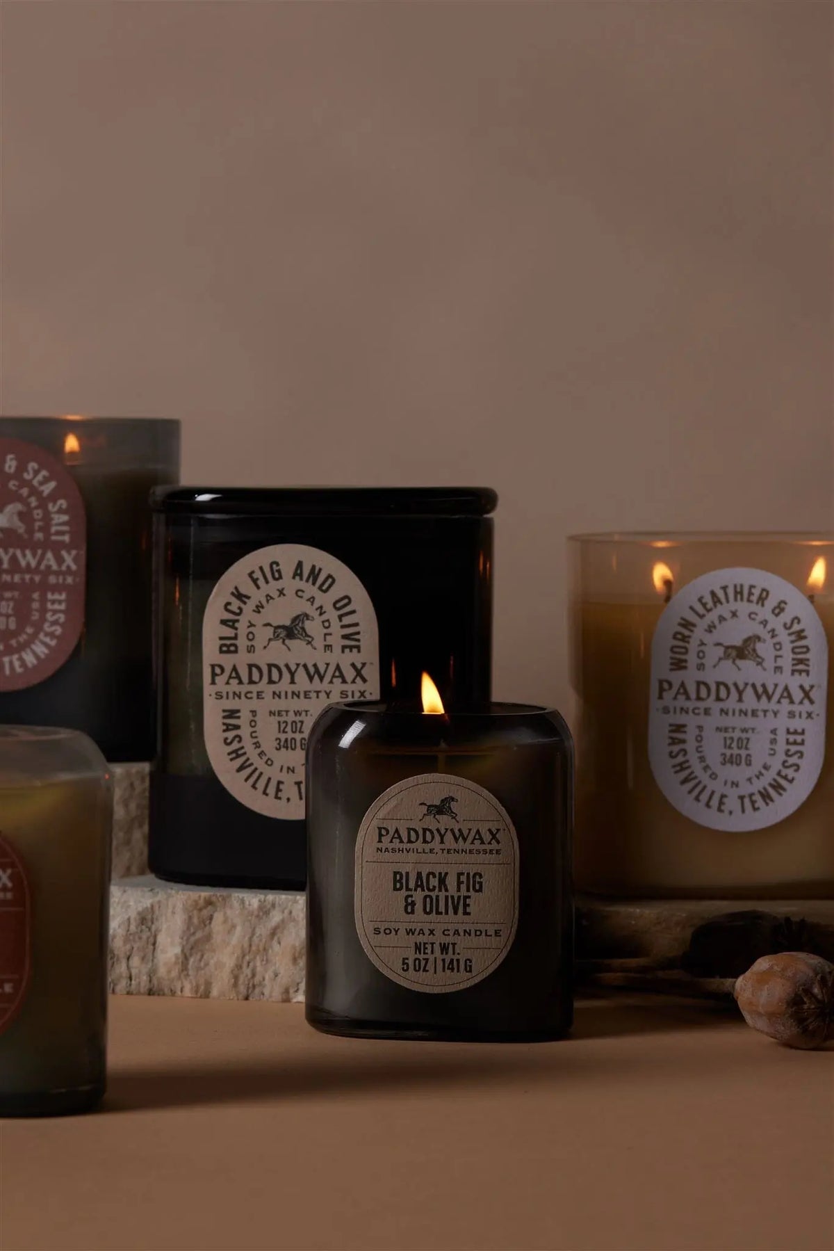 The Black Fig & Olive - Vista 5 oz Candle adds a luxurious scent and modern style to any space, arranged on a stone surface against a beige backdrop—perfect for contemporary home decor.