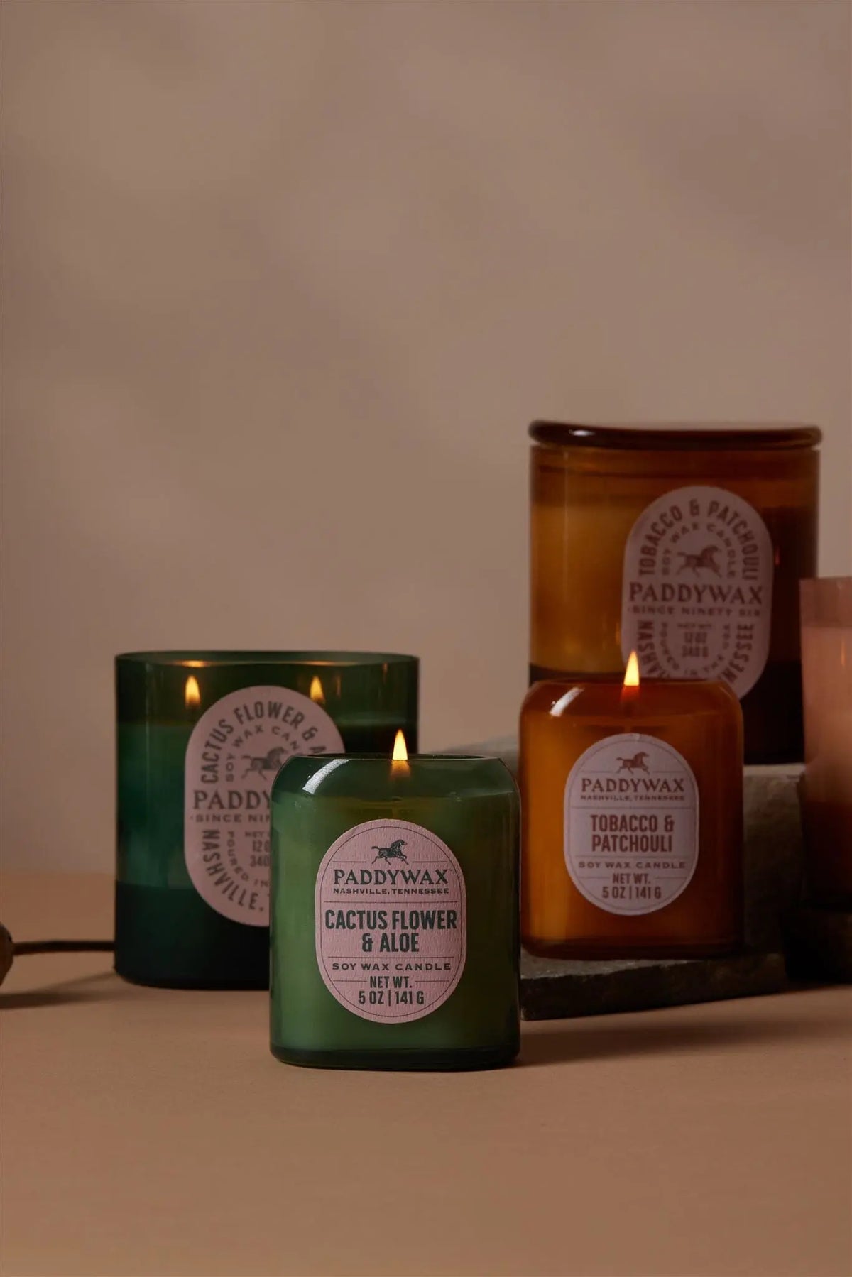 Four lit Cactus Flower & Aloe Vista 5 oz candles in green glass containers are arranged on a neutral background, bringing a touch of modern home decor with their luxurious fragrance.