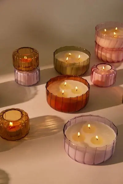 A Salted Iris - Ripple 4.5 oz Candle and other vintage candles in colored glass containers of different sizes are arranged on a flat surface, casting soft shadows.