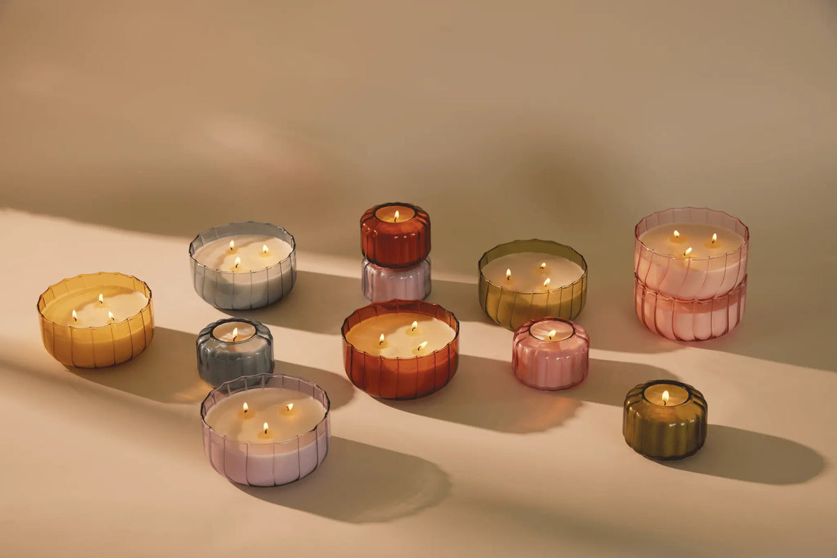 Desert Peach - 12 oz Candles in vintage colored glass holders are arranged on a beige surface, casting soft shadows in natural light.