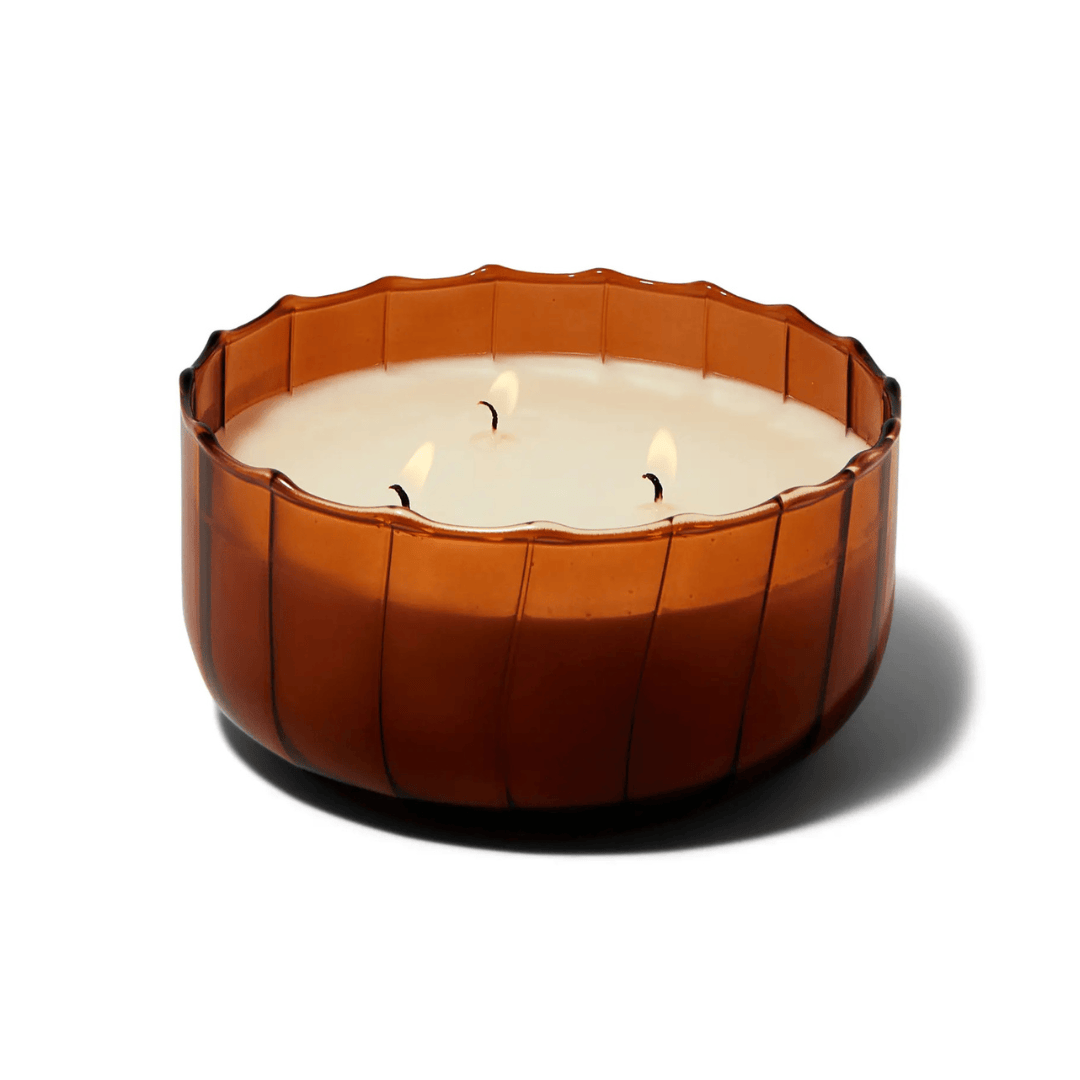 The Tobacco Patchouli - Ripple 12 oz Candle features a brown, round ribbed glass holder with creamy white wax and three lit wicks, evoking vintage colored glass against a white backdrop.