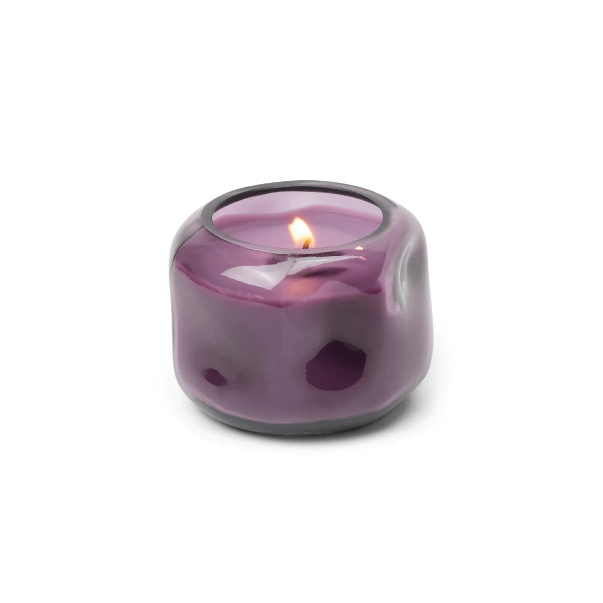 A small, round, purple glass candle holder houses the Violet & Vanilla - Basalt 5 oz Candle, its warm flame casting a gentle glow and filling the air with violet and vanilla scents.